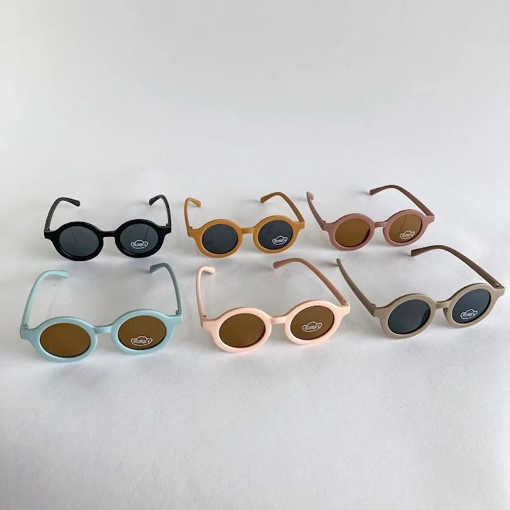 Set of six pairs of children's sunglasses in different colors on a light gray background