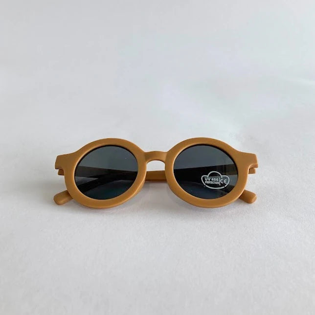 Round kids sunglasses with mustard yellow frame and dark lenses on a light gray background