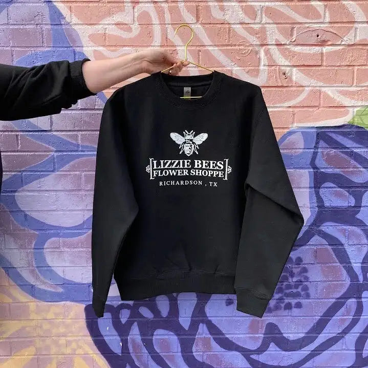 Black sweatshirt with 'Lizzie Bees Flower Shoppe' logo on a colorful brick wall background