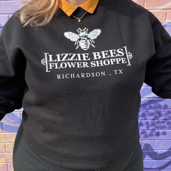 Black sweatshirt with 'Lizzie Bees Flower Shoppe' logo worn by a person, against a colorful wall.