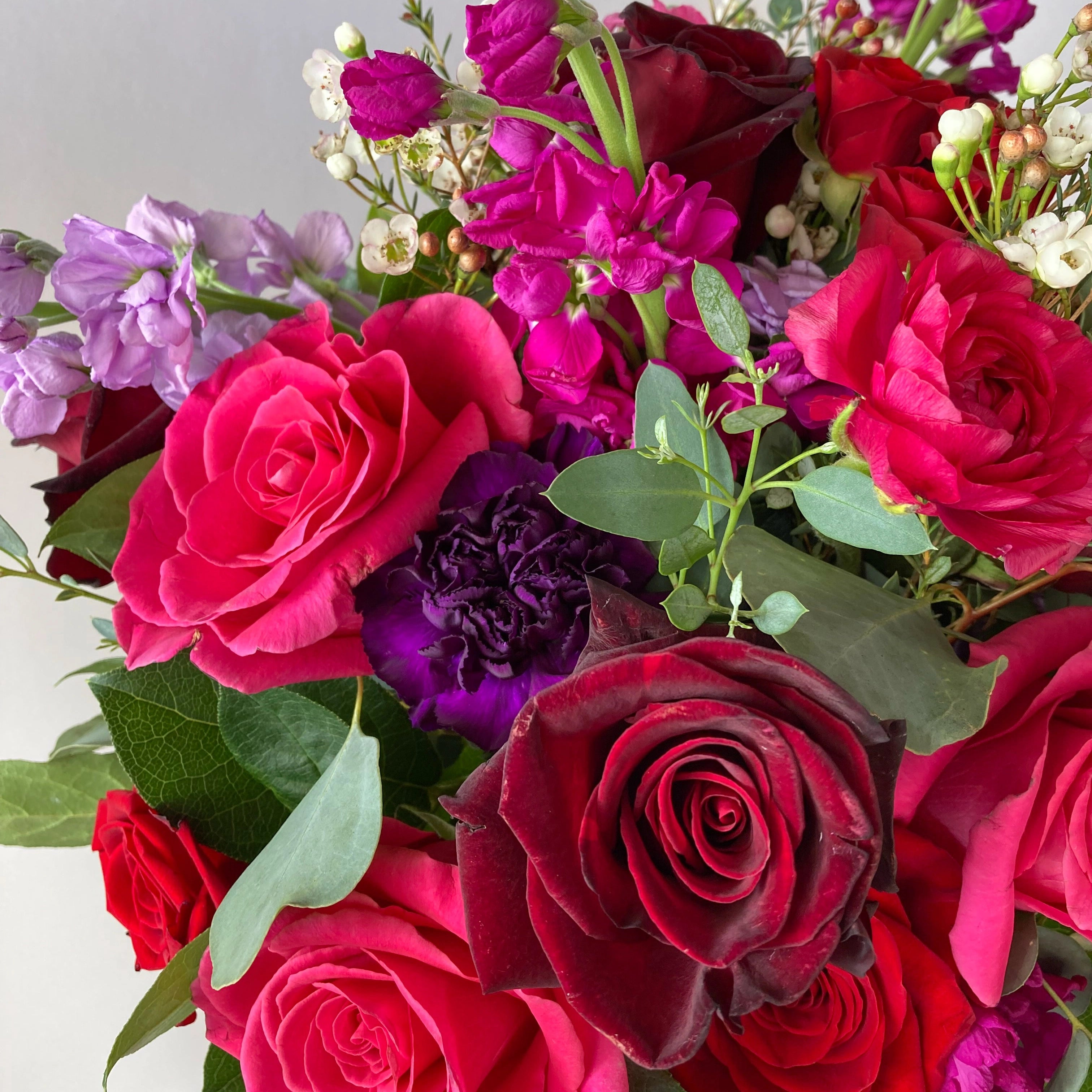 Bouquet of red and pink roses with greenery on a light gray background