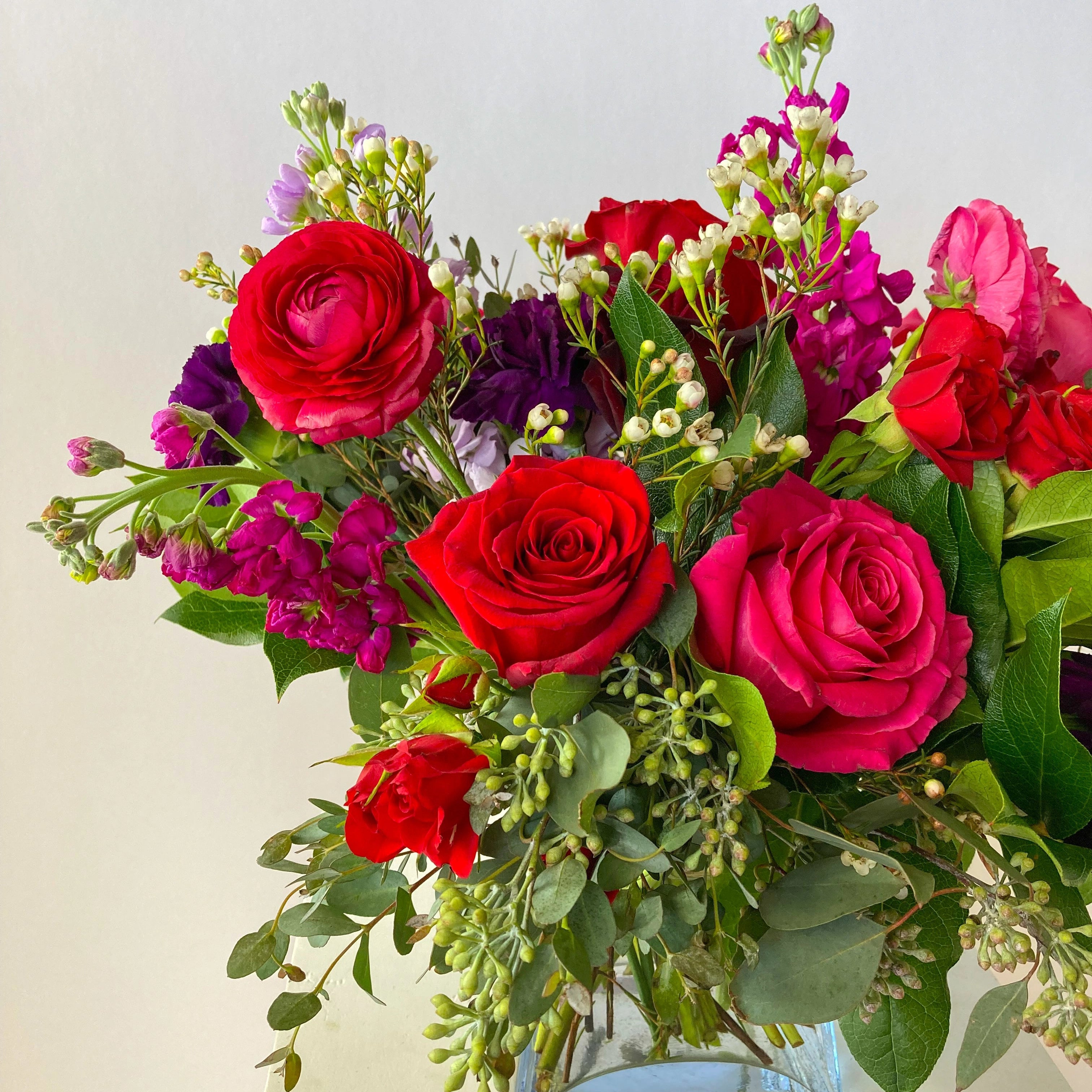 Bouquet of red and pink roses with greenery in a clear vase on a light background