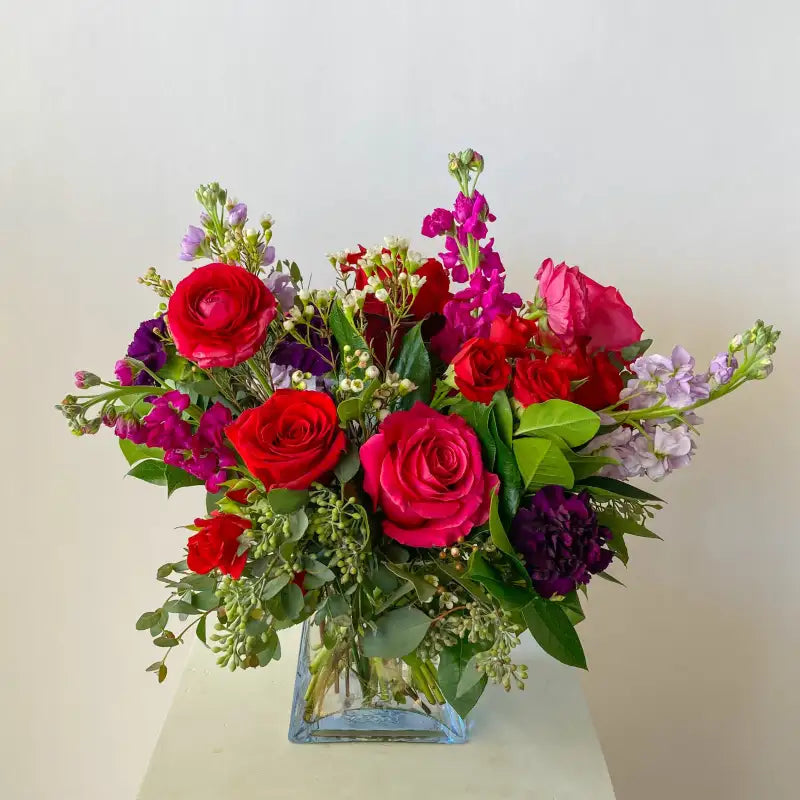 Bouquet of red, pink, and purple flowers in a clear vase on a light background
