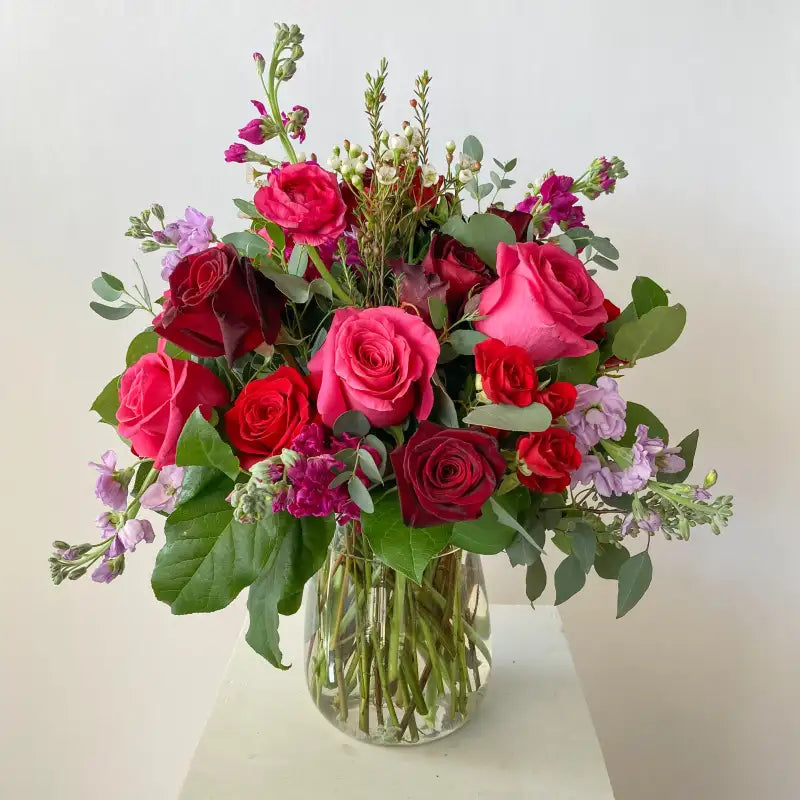 Bouquet of red and pink roses with greenery in a clear vase on a light background