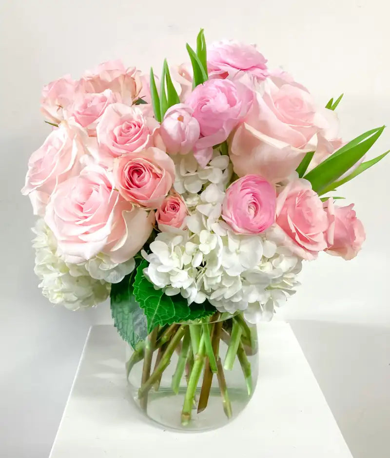 Bouquet of pink roses and white hydrangeas in a clear vase on a white background