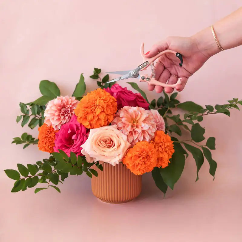Person holding scissors next to a colorful flower arrangement on a pink background