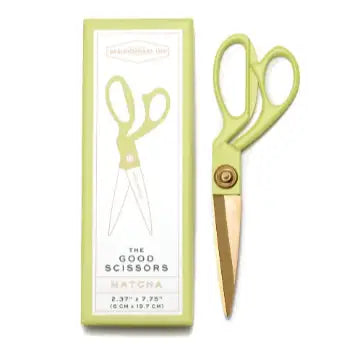 Green scissors with gold blades in front of their packaging on a white background