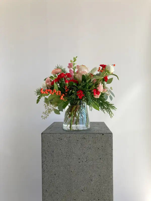 Bouquet of flowers in a clear vase on a gray pedestal against a white background