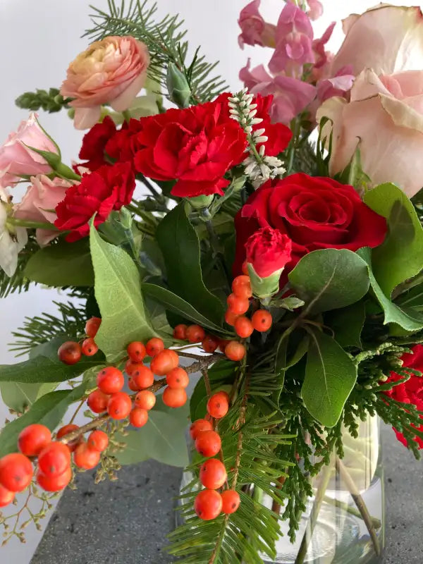 Bouquet of red and pink roses with greenery and berries in a clear vase.