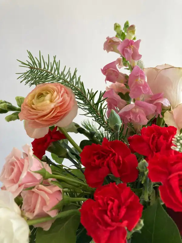 Bouquet of red, pink, and peach flowers with greenery on a light background