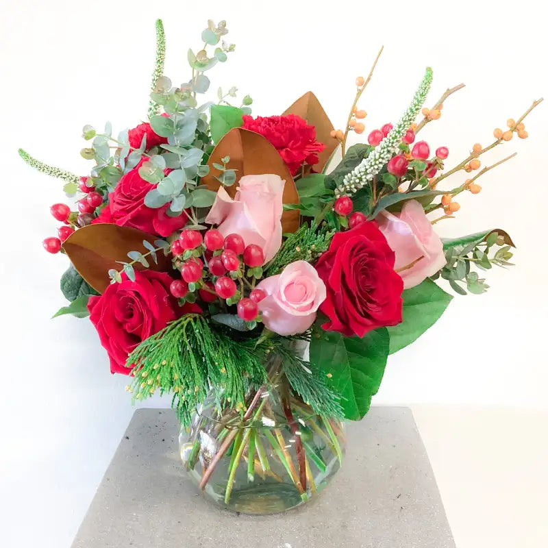 Bouquet of red and pink roses with greenery in a clear vase on a white background