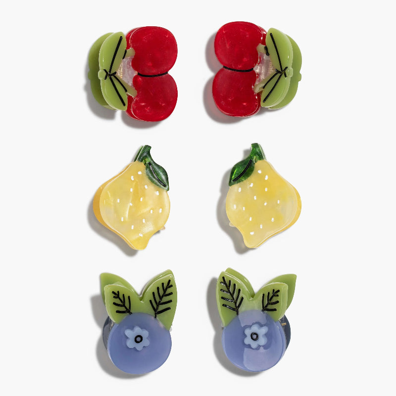 Six small fruit and flower hair clips arranged in two columns on a light gray background. The top pair resembles red cherries with green leafy sides, the middle pair are yellow lemons, and the bottom pair are lavender-blue flowers with green leaves.