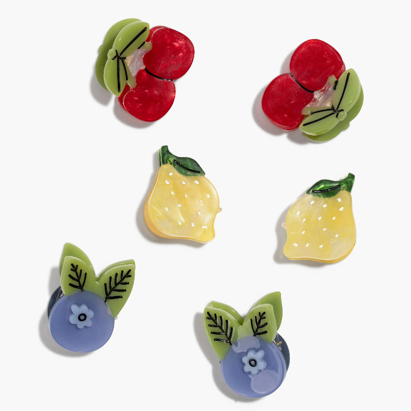 Six colorful fruit-shaped hair clip accessories arranged on a plain white background, including red cherries, yellow lemons, and blue blueberries with green leaves.