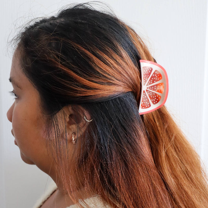 Person with a ponytail using a hair tie shaped like a grapefruit slice against a white background