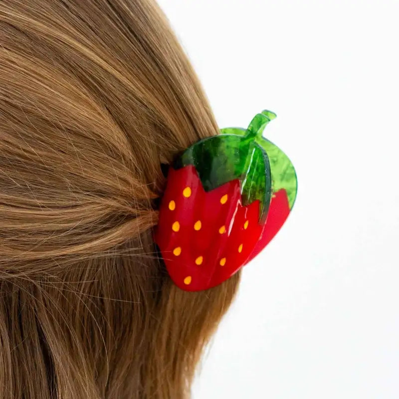 Strawberry-shaped hair clip on a person's hair against a white background
