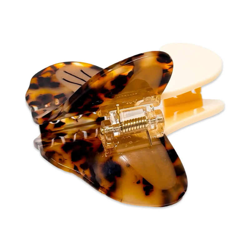 A tortoiseshell hair claw clip with a cream-colored inner clip and a clear plastic hinge, shown on a solid white background.