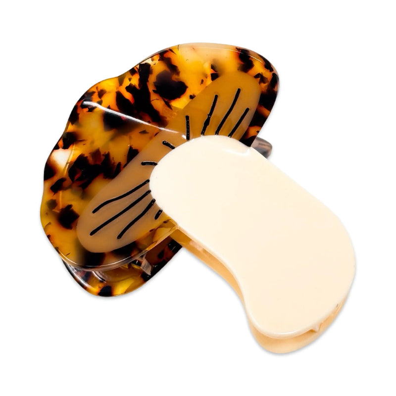 A hair claw clip shown open on a plain white background, with a translucent tortoiseshell-patterned outer piece and a smooth cream-colored inner piece.