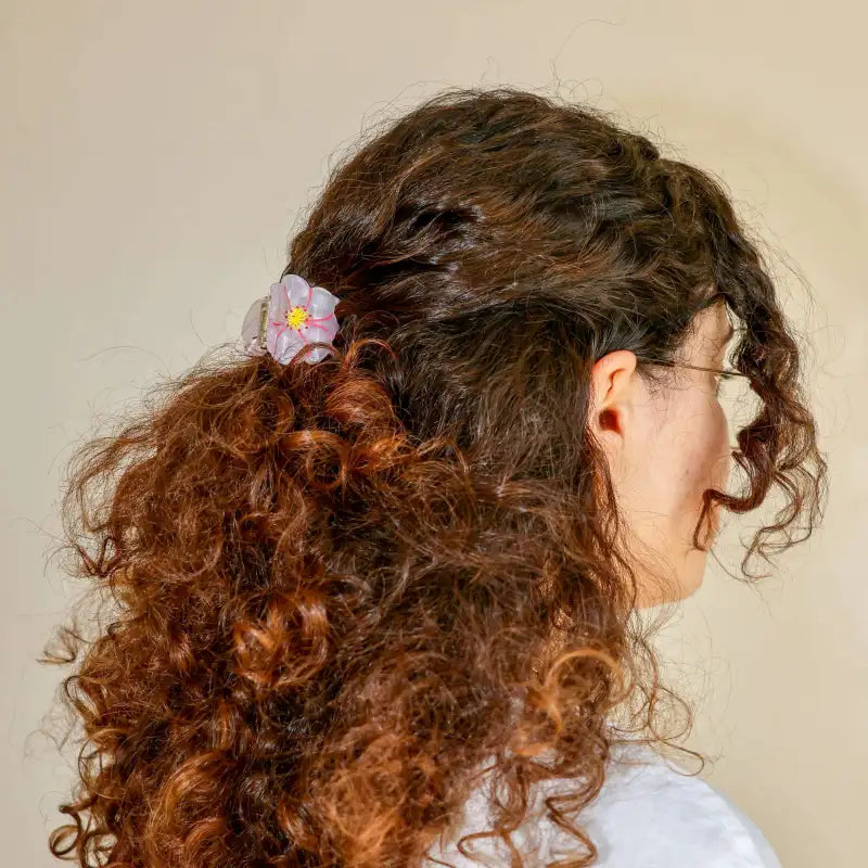 Person with curly hair wearing a flower clip against a plain background