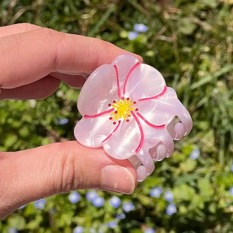 Hand holding a pink flower-shaped hair clip with a blurred green background