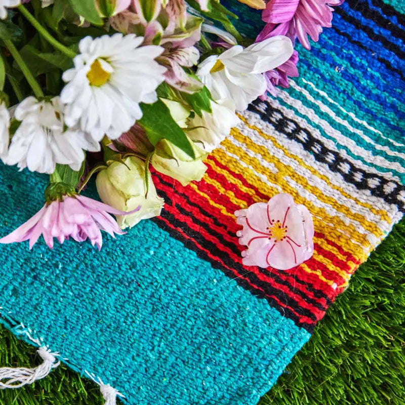 Colorful woven mat with flowers on a grassy background