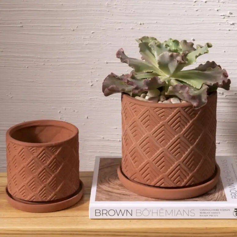 Two terracotta planters with geometric patterns on a wooden surface.