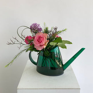 Green watering can with pink roses and greenery on a white surface