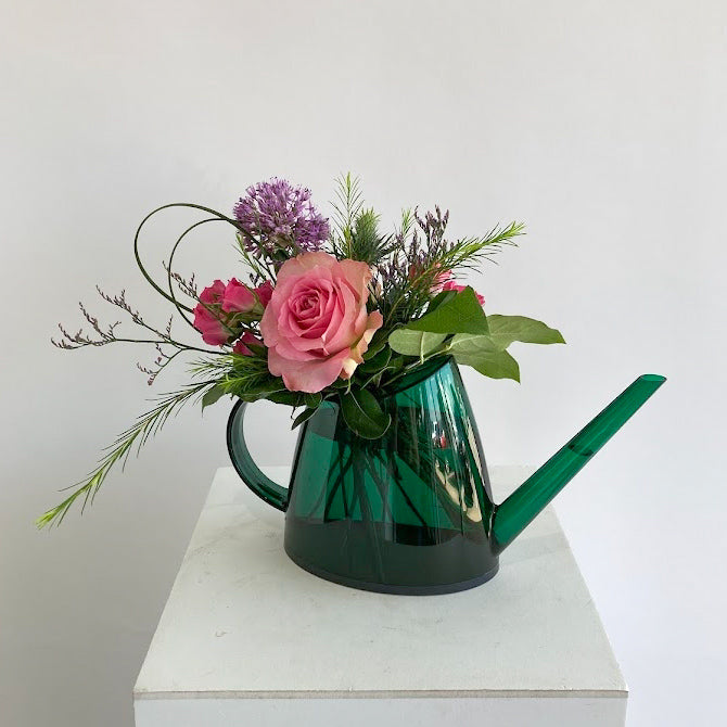 Green watering can with pink roses and greenery on a white surface