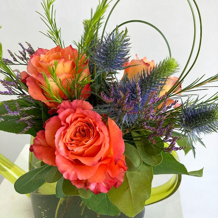 Bouquet of orange roses and greenery in a green watering can on a white background