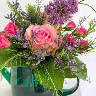 Bouquet of pink roses and purple flowers in a green watering can on a white background