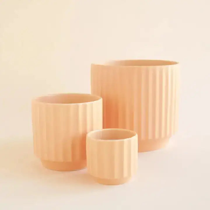 Three peach-colored ceramic planters of different sizes on a light beige background