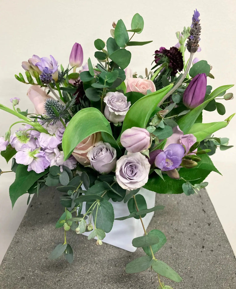 Bouquet of flowers with greenery in a white box on a concrete surface.
