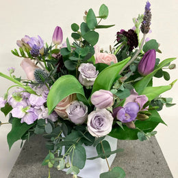 Bouquet of flowers with greenery in a white box on a concrete surface.