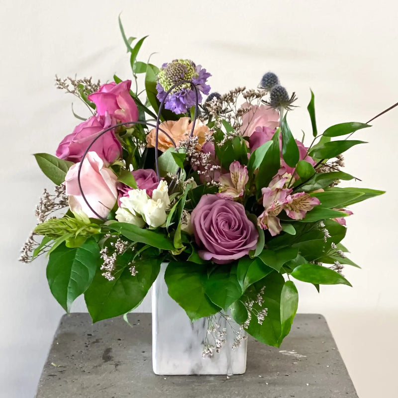 Bouquet of flowers in a clear vase on a gray surface with a white background