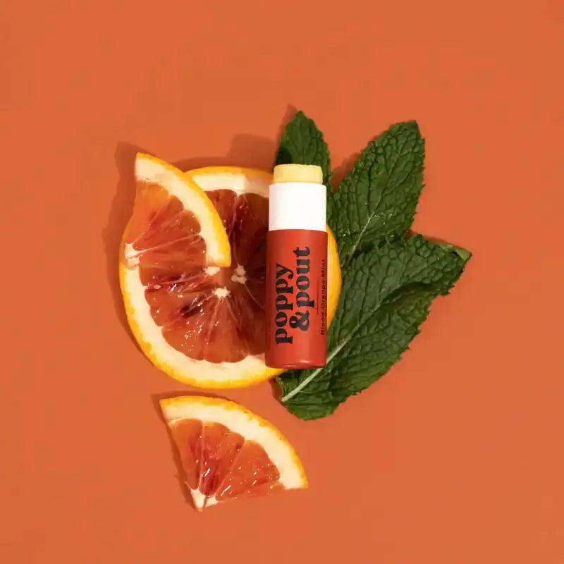 Lip balm with orange slices and mint leaves on an orange background