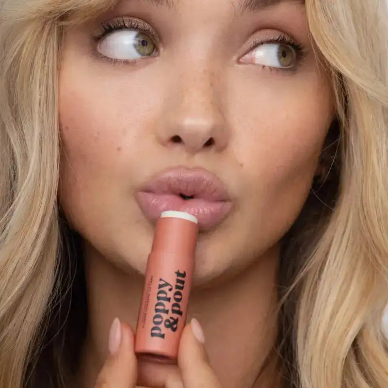 Woman holding a pink lip balm with 'Poppy & Pout' branding.