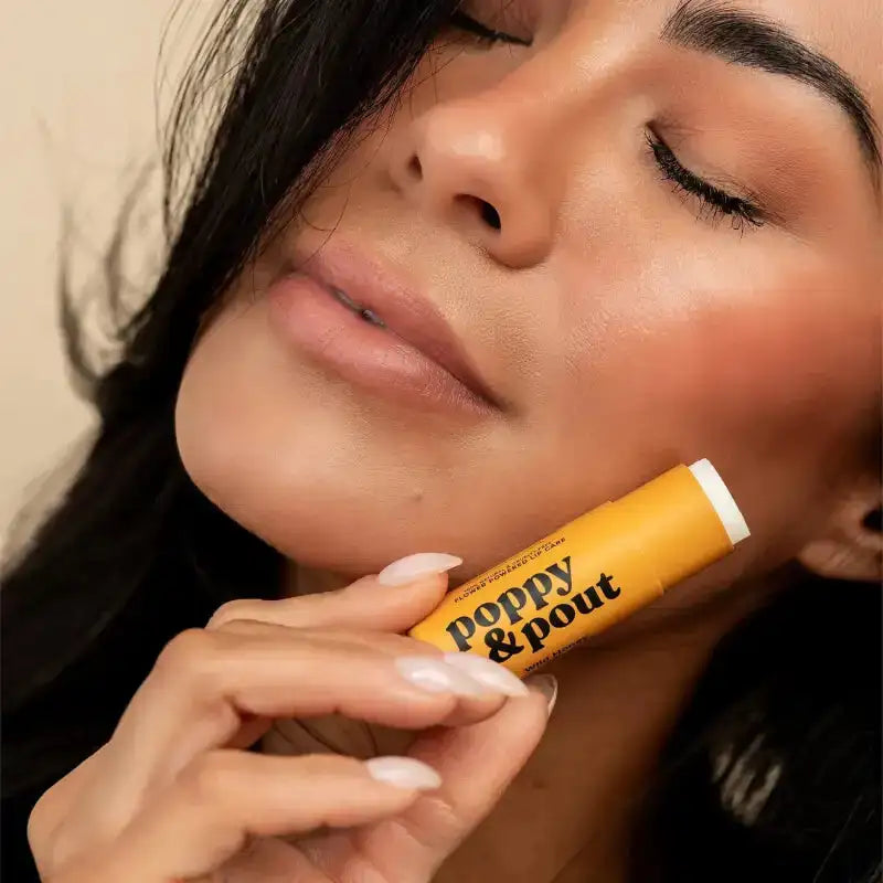 Woman holding a 'Poppy & Pout' lip balm close to her face