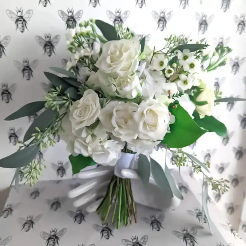Close up of white floral nosegay bouquet with small white blossoms, green leaves, and natural texture