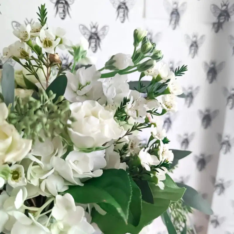 White nosegay bouquet with layered white blooms, delicate filler flowers, and soft green foliage