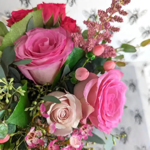 Close up of pink nosegay bouquet with roses, berry accents, textured greenery, and soft blush tones