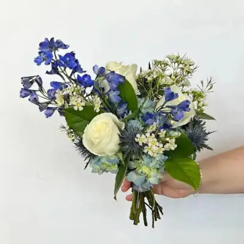 Blue and white nosegay bouquet with white roses, blue thistle, pale blue flowers, and greenery