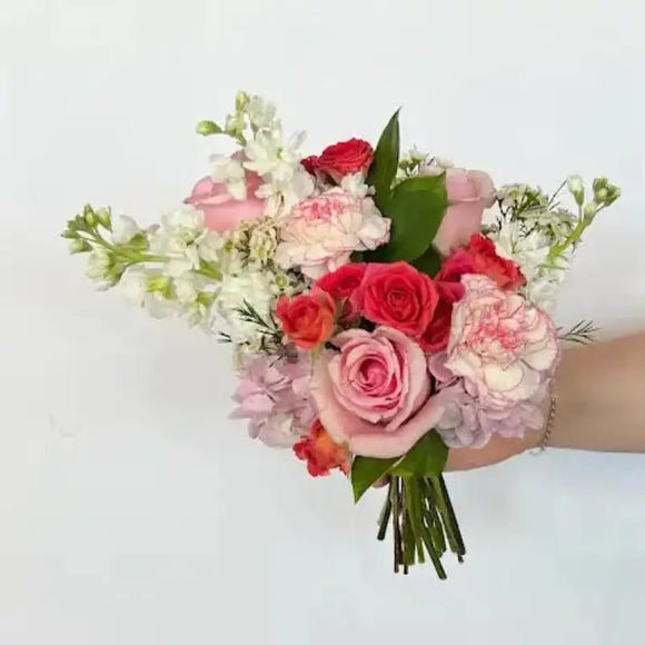 Hand held nosegay bouquet with soft pink roses, blush carnations, white blooms, and green foliage
