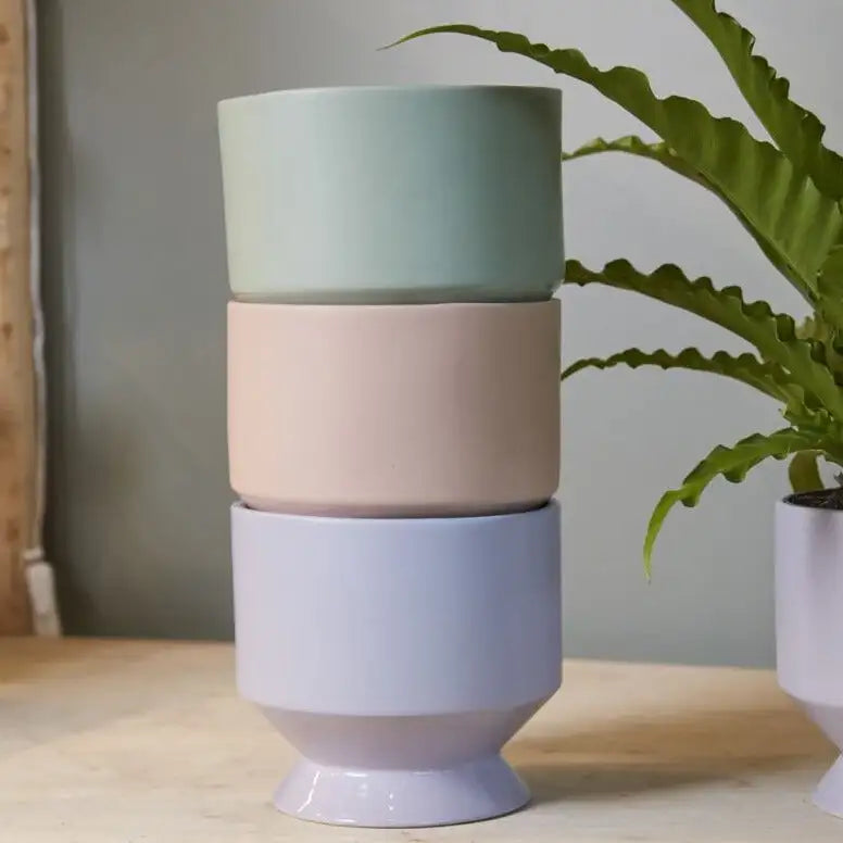 Stacked ceramic planters in pastel colors on a wooden surface with a plant in the background.