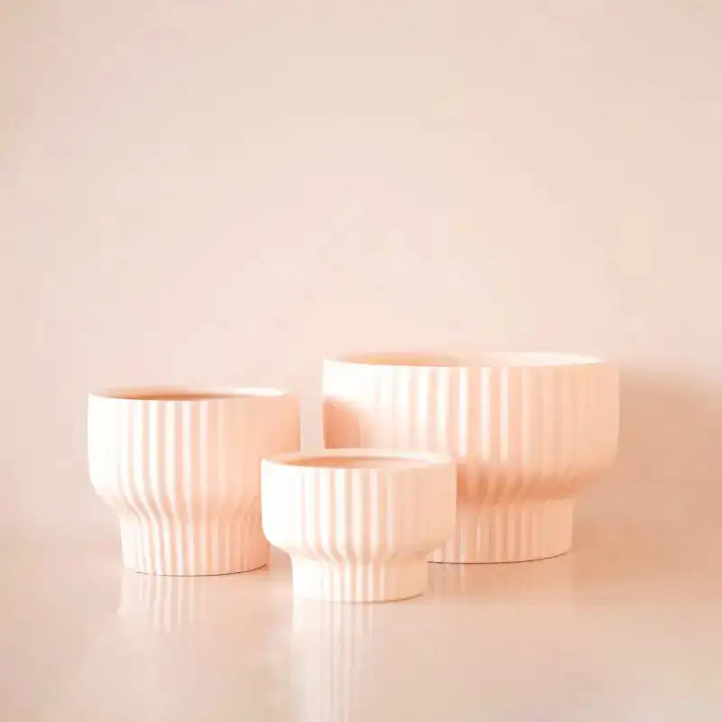 Three ceramic planters of different sizes on a light pink background