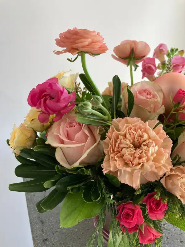 Bouquet of pink, red, and yellow flowers with green leaves on a light gray background