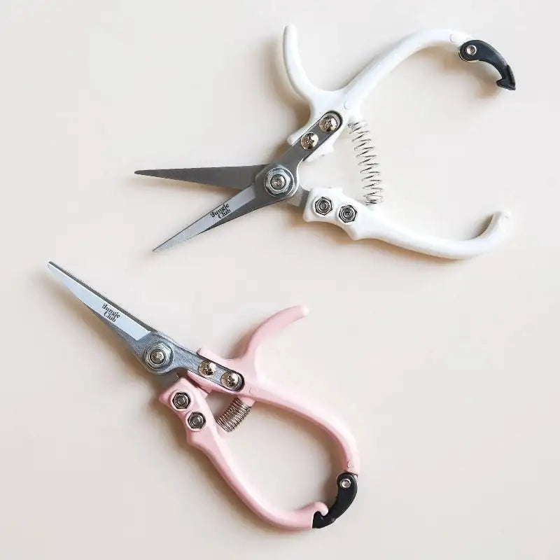 Two pairs of scissors, one pink and one white, on a light background