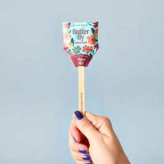 Hand holding a butterfly seed pop with a colorful label against a light blue background