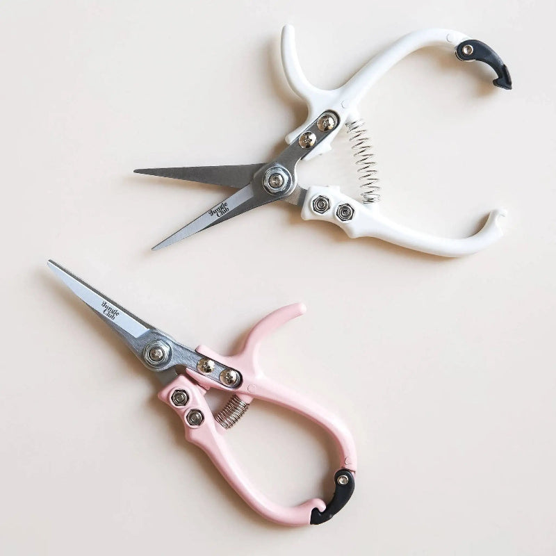 Two pairs of scissors, one pink and one white, on a light beige background.