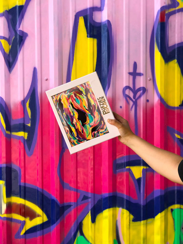 Person holding a colorful abstract painting against a vibrant, abstract-patterned wall.