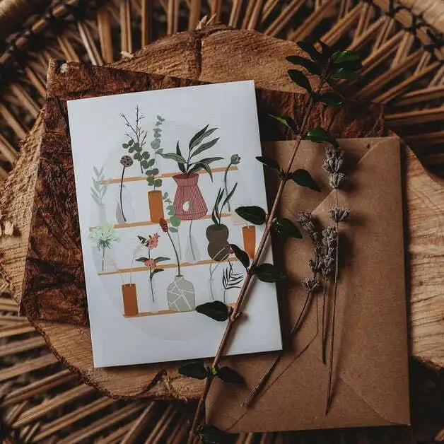 Greeting card with plant illustrations on a wooden surface with dried plants.