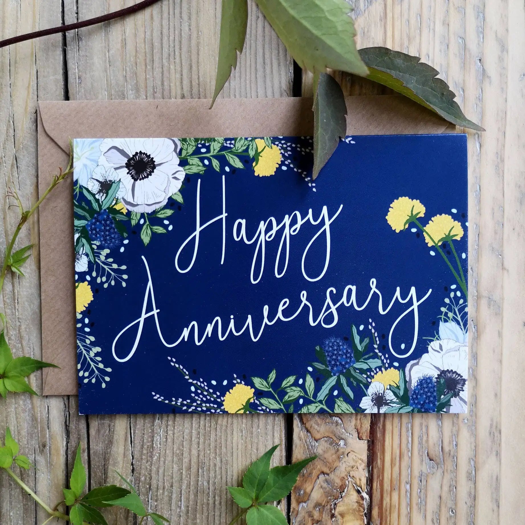 Navy blue card with floral designs and 'Happy Anniversary' text on a wooden surface.